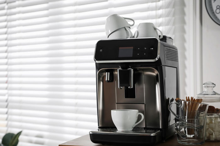 Coffee machine with cups on top, set against a window backdrop in a friend's home.