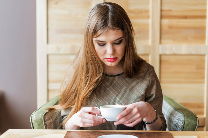 A woman looking at a cup, appearing displeased, in a coffee discussion setting without actually having coffee.