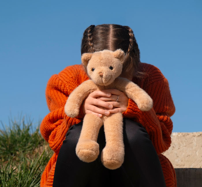 Girl with leukemia holding teddy bear tightly, sitting outdoors in orange sweater on a sunny day. Girl with leukemia holding teddy bear tightly, sitting outdoors in orange sweater on a sunny day.