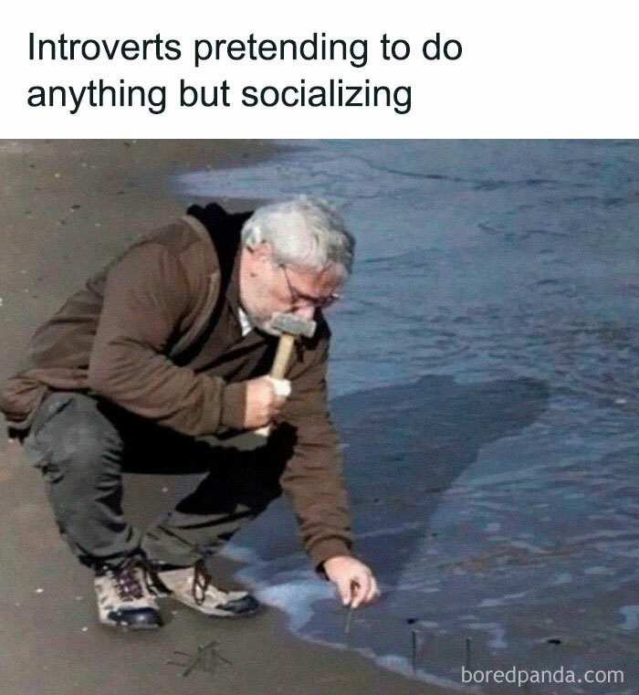 Man kneeling on beach, pretending to hammer nails into the sand, capturing introverts’ socially exhausted moments.
