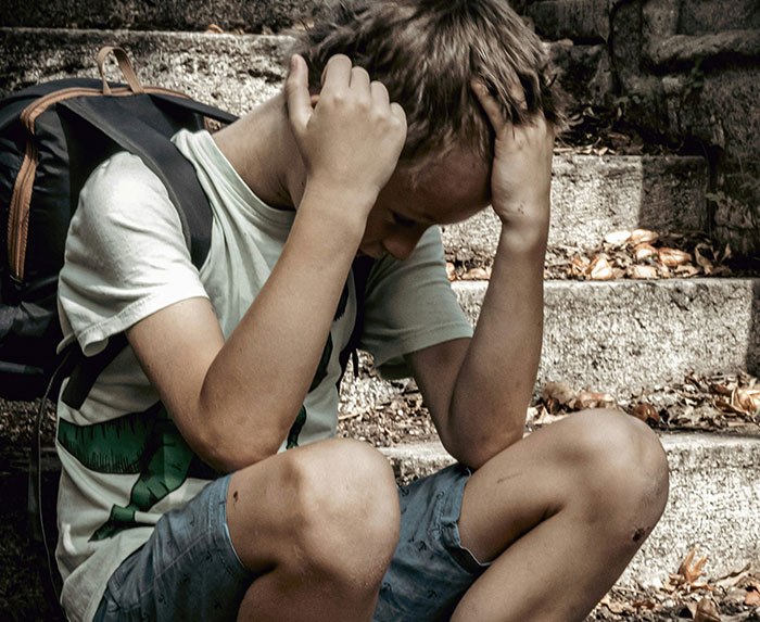 Child sitting on steps, visibly upset, with hands on head, wearing a backpack. Child sitting on steps, visibly upset, with hands on head, wearing a backpack.