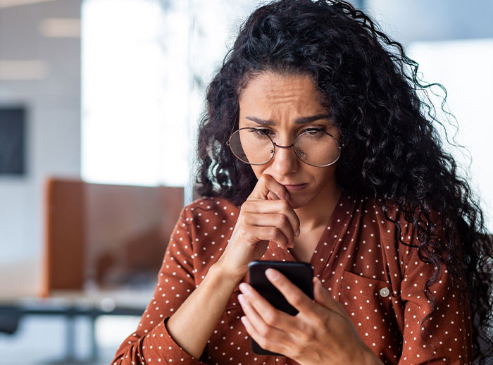 A concerned woman with glasses looks at her phone, highlighting eating disorder awareness and online implications. A concerned woman with glasses looks at her phone, highlighting eating disorder awareness and online implications.