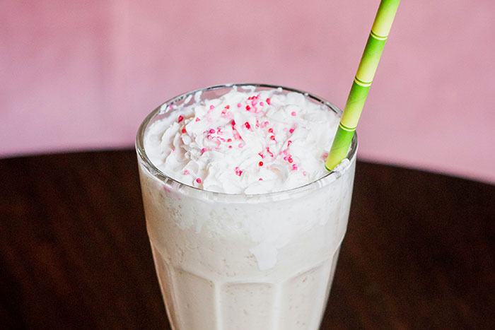 Milkshake topped with whipped cream and sprinkles, served in a classic glass with a striped straw.