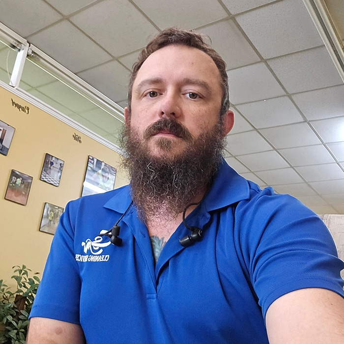 Bearded man in a blue shirt sitting indoors in a restaurant.