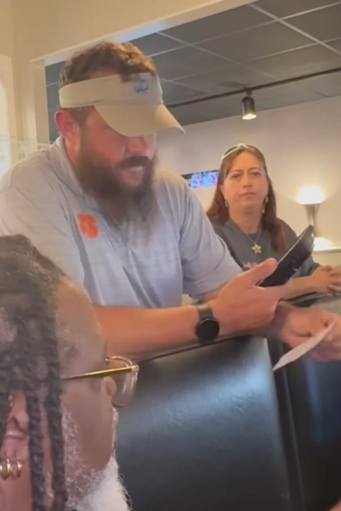 Restaurant owner reading a note, holds a phone; staff looks on, highlighting unprofessional customer-shaming incident.