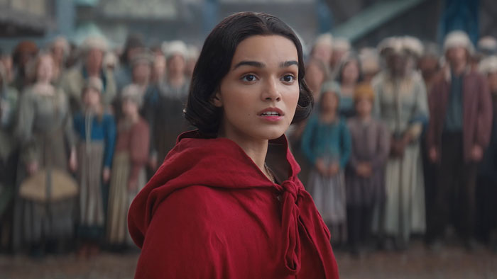 Young woman in a red hood in a crowded medieval village, related to Snow White mock controversy.
