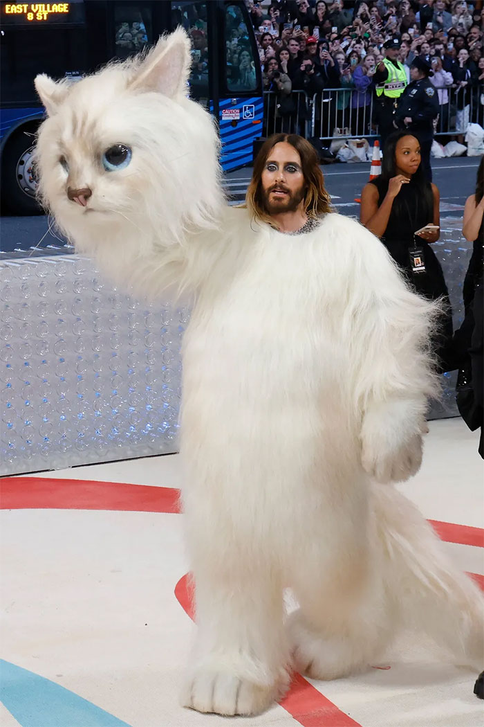 Celebrity in an elaborate oversized white cat costume with dramatic makeup at the Met Gala fashion event.