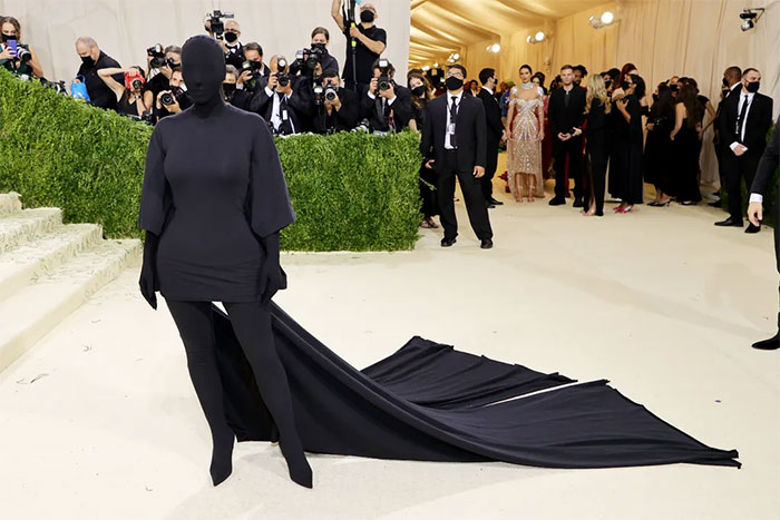 Celebrity dressed in fully covered black outfit with long train posing on the red carpet at Met Gala event.