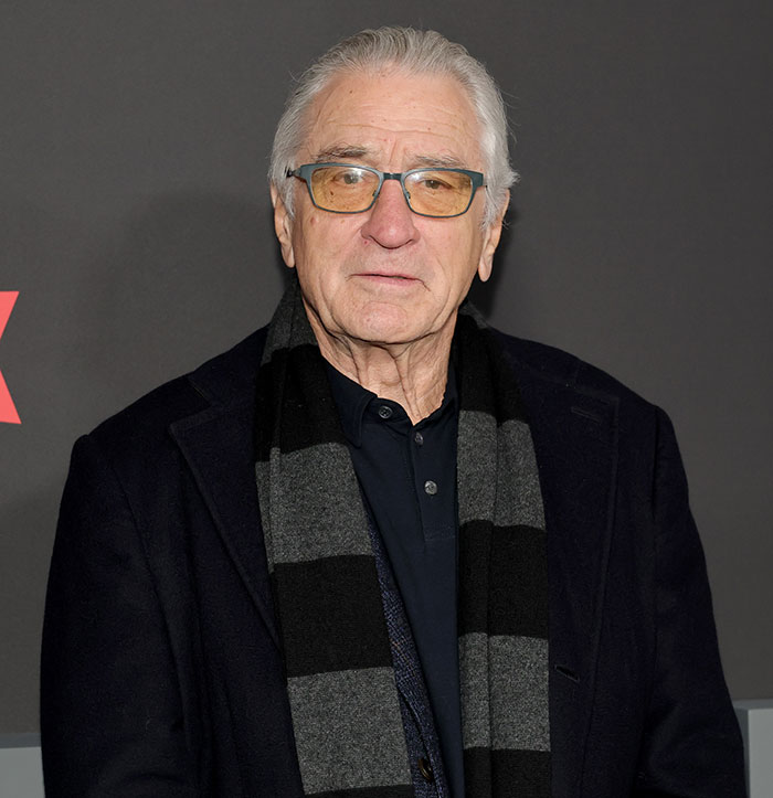 Robert De Niro wearing glasses and a dark coat and scarf at a public event, related to his daughter coming out as transgender. Robert De Niro wearing glasses and a dark coat and scarf at a public event, related to his daughter coming out as transgender.