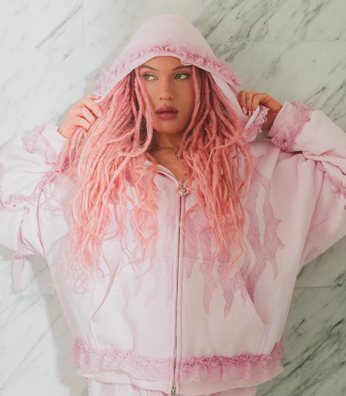 Robert De Niro's daughter with pink dreadlocks in a pink hoodie, posing against a marble wall, representing transgender identity. Robert De Niro's daughter with pink dreadlocks in a pink hoodie, posing against a marble wall, representing transgender identity.