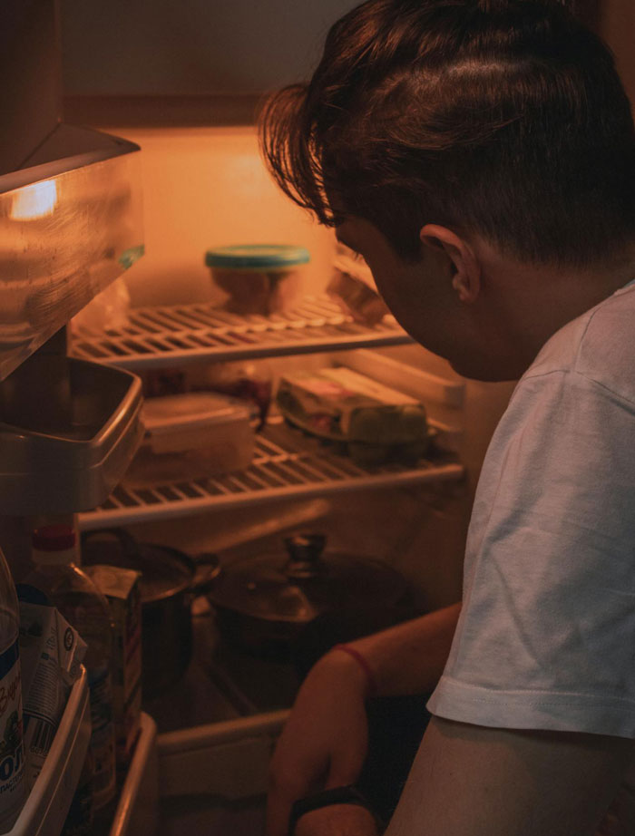 Man looking into fridge at night, thinking of horse meat as revenge on roommate for stealing food.