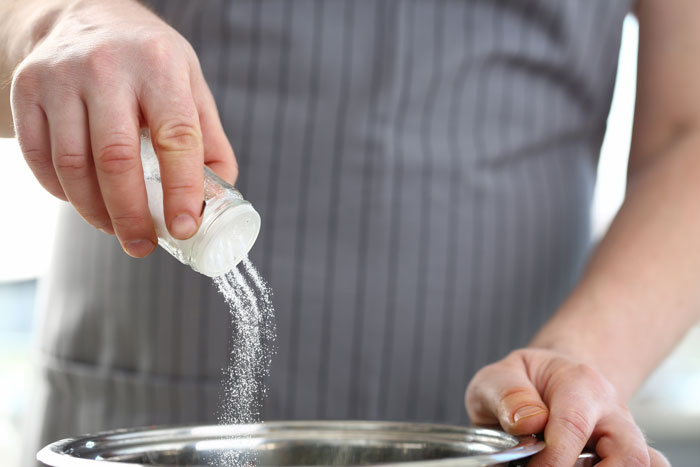Woman adding salt to a dish while cooking for boyfriend's family on vacation.