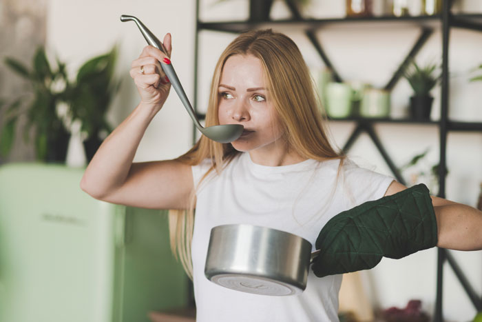 Woman cooking in kitchen with ladle and pot, appearing frustrated during family vacation meal preparation.