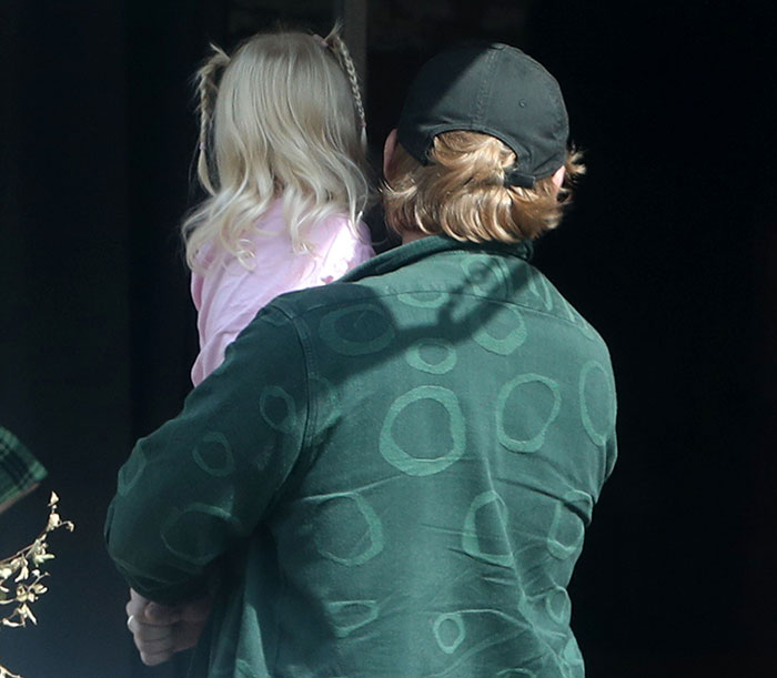 Rupert Grint holds his daughter, wearing a pink outfit, against a dark background.