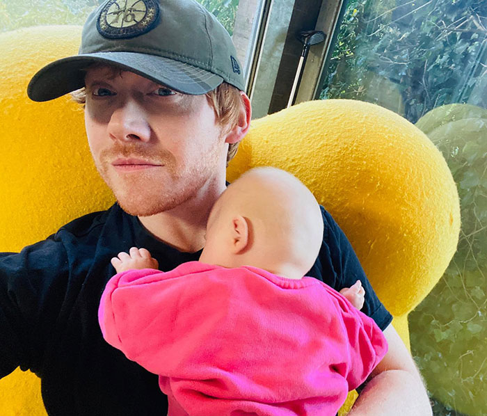 Actor Rupert Grint with his baby daughter in a cozy home setting, displaying new fatherly joy.