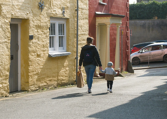 Person and child holding hands on a sunny street, illustrating safety tips.