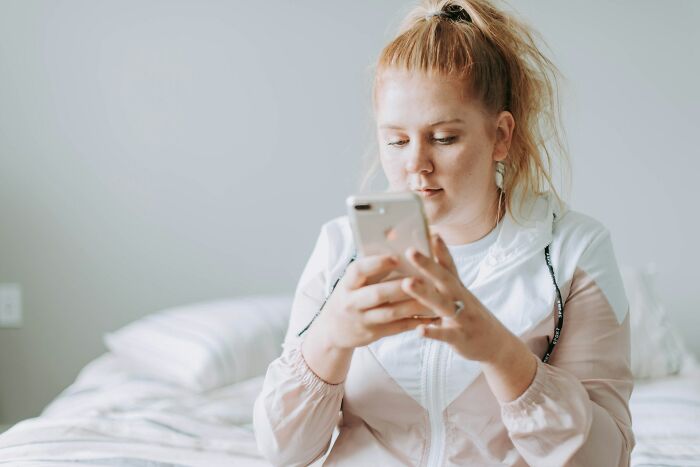 Woman pondering relationship decision, sits on bed with phone, reflecting on partner's actions.
