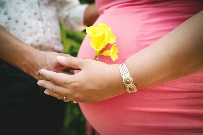 Pregnant woman in a pink dress holding yellow flowers with hands gently touching, reflecting experiences in church.