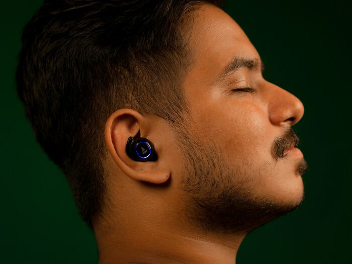 Young man with wireless earbuds, eyes closed, appearing calm while reflecting on unexplainable pain people are enduring.