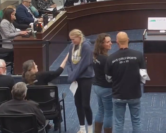 A board meeting with a girl's testimony on the trans locker room, showing emotional reactions from attendees.