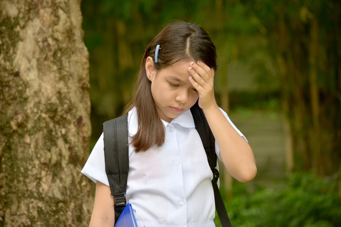 Young girl in school uniform looking upset outdoors, holding her head. Young girl in school uniform looking upset outdoors, holding her head.