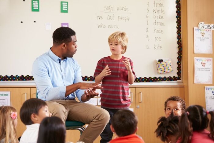 Child comedian explaining a funny story to teacher and classmates in a classroom setting.