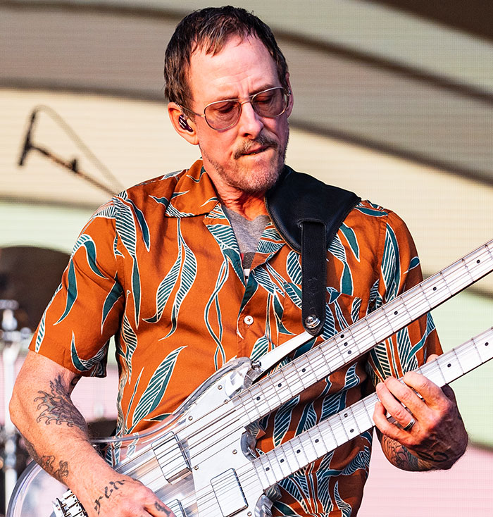 Musician playing double-neck guitar on stage during performance.