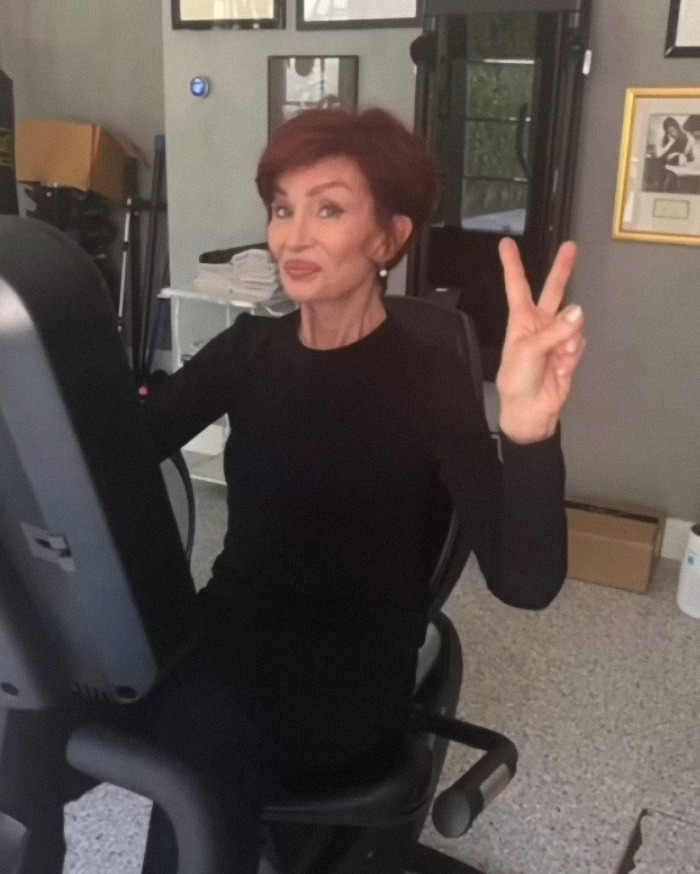 Woman on exercise bike, smiling and gesturing peace sign, amidst filter controversy in family photo.