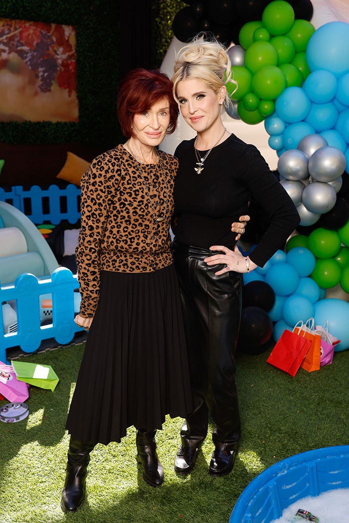 Sharon Osbourne and another person at a colorful outdoor event, standing on grass with balloons in the background.