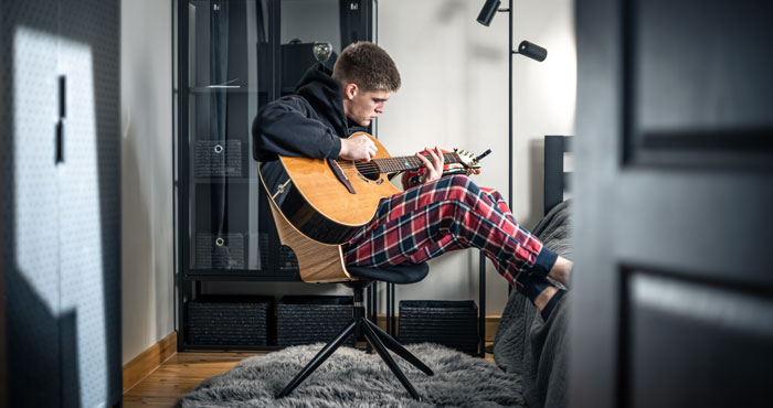 Young man playing guitar, wearing plaid pajama pants, enjoying solitude at home. Young man playing guitar, wearing plaid pajama pants, enjoying solitude at home.