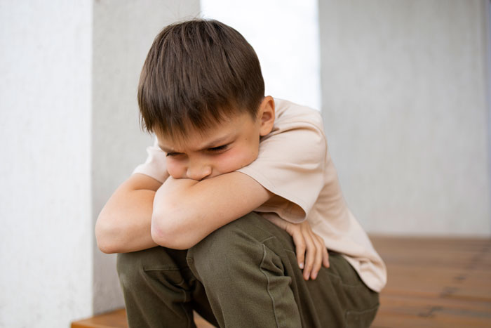 A young boy sitting sadly, resting his head on folded arms, reflects custody issues.