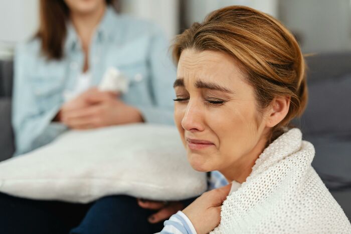 A woman looking upset, wrapped in a blanket, with another person in the background, reacting to family exclusion at a wedding.