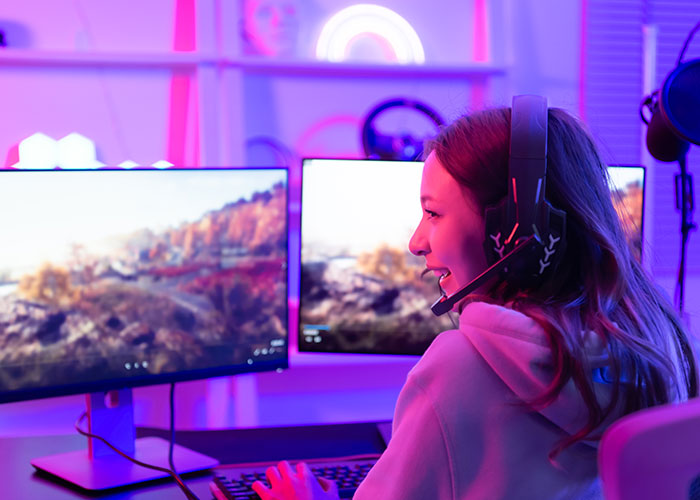 Woman gaming on a computer in a room with neon lights, wearing headphones.