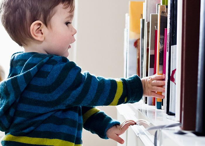 Toddler reaching for books on a shelf, leading to family drama and damages.