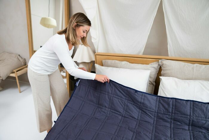 A woman tidying a bed, illustrating strict cleaning rules with a blue comforter and neutral bedroom decor.