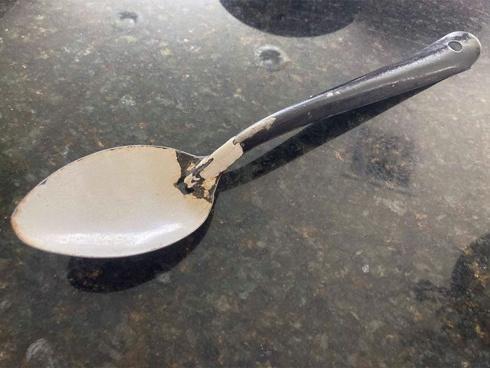 Worn and damaged metal spoon on a dark surface, illustrating potential danger in daily utensils.