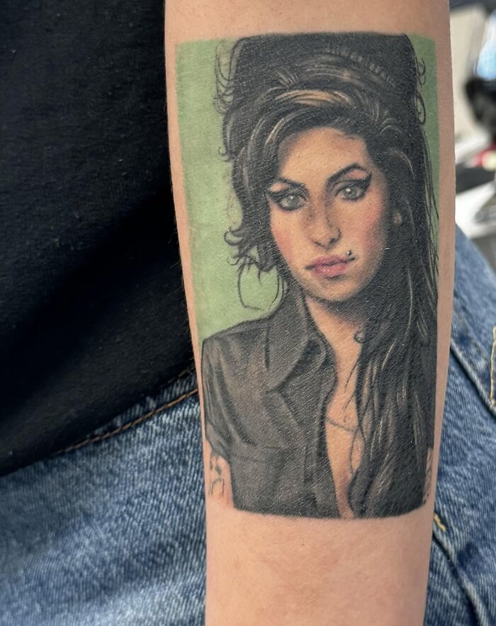 Tattoo of a woman with dark hair and piercing on someone's arm, showcasing a vivid artistic style.