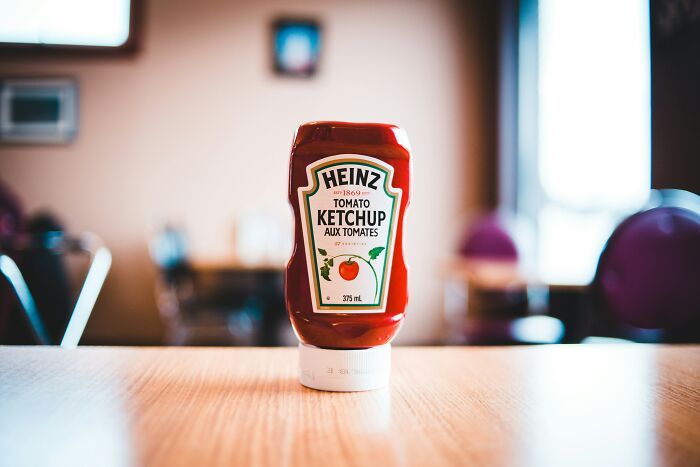 A bottle of Heinz ketchup on a wooden table with bright indoor lighting, representing legal things with unusual vibes.