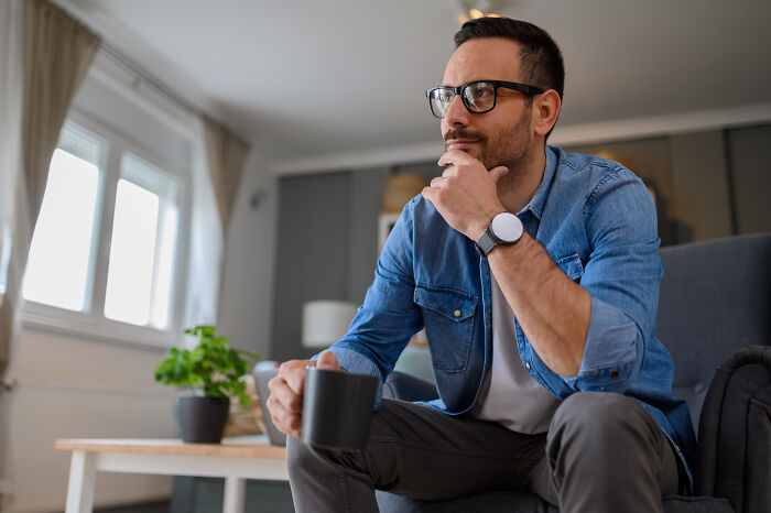 Man in a blue denim shirt and glasses holding a mug, sitting thoughtfully, reflecting on legal things with psychopath vibes.