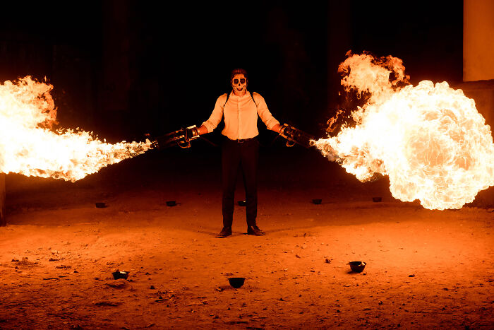 Person with face paint creating large flames in a dark setting, giving off intense vibes.