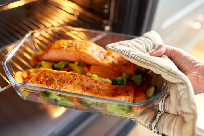 Salmon and vegetables in glass dish being placed in oven, depicting oddly legal cooking choices.