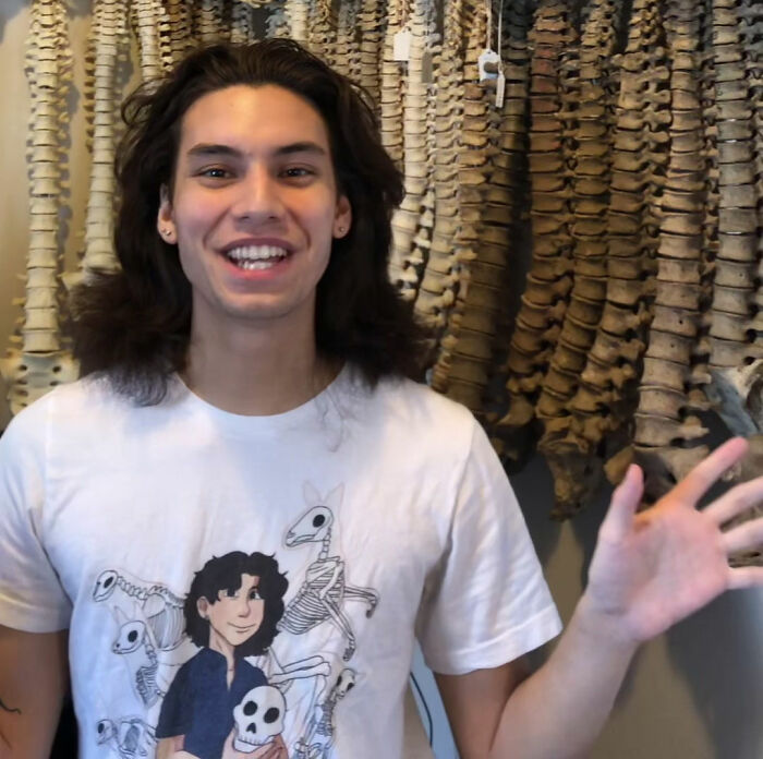 Young person smiling, wearing a skeleton-themed shirt, in front of a background of animal bones. Psychopath vibes theme.