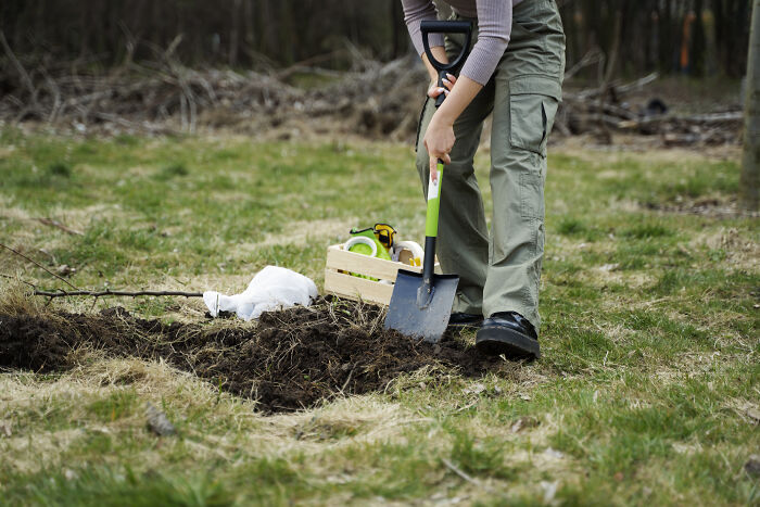 A person digging in a field, giving off unusual vibes, with a shovel and crate nearby.