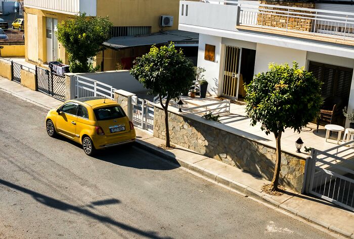 Yellow car parked across two spaces on a sunny residential street, showing wildly legal parking that gives psychopath vibes.