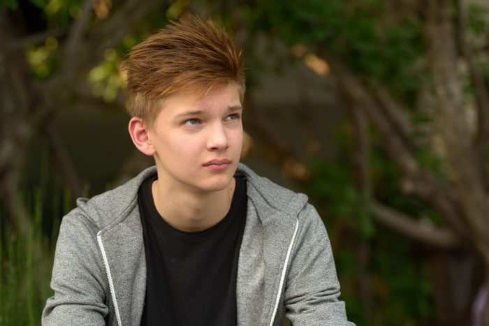 Teen boy in gray hoodie sitting outdoors, illustrating dad catching teen son creeping around neighbor&rsquo;s yard at night.