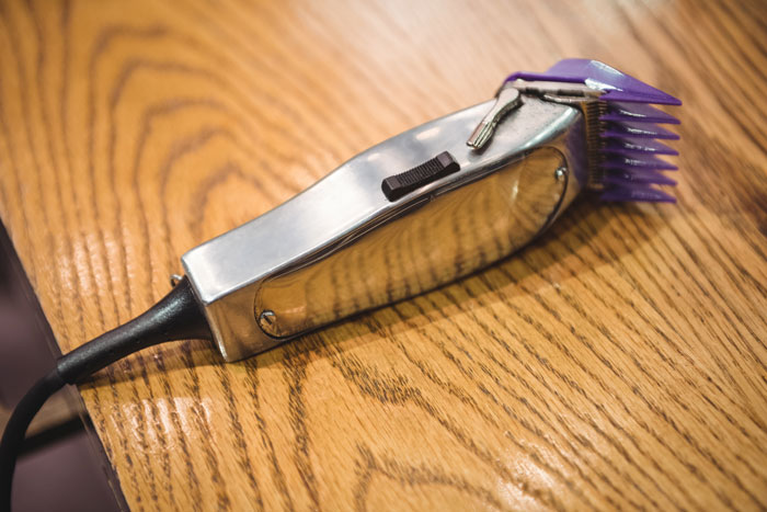 Electric hair clipper with purple attachment resting on a wooden surface, related to son father grooming drama.