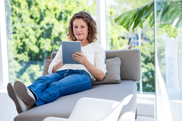 Woman relaxing on sofa with a tablet, illustrating an explain-adult-moments concept.