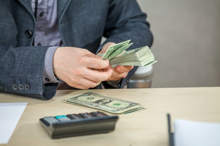Person counting dollar bills at a desk, illustrating adult financial moments and responsibilities.