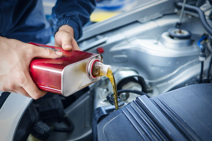 Pouring oil into a car engine, illustrating common adult tasks and explain-adult-moments, in a maintenance setting.