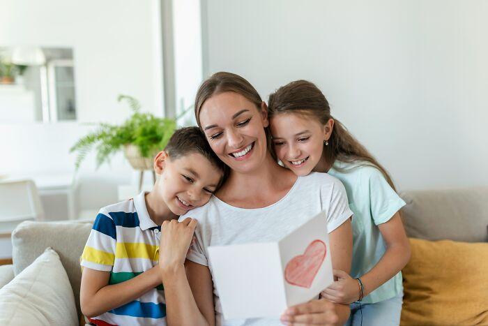 Smiling woman enjoying heartfelt card with two children, illustrating adult moments.